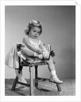 1960s little girl putting on shoes sitting on chair by Anonymous