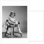 1960s little girl putting on shoes sitting on chair by Anonymous