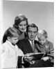 1960s family father mother sons reading book together by Anonymous