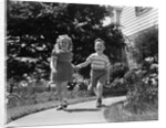 1950s two children holding hands smiling walking along sidewalk by Anonymous