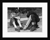 1950s teen boy helping girl put on metal roller skates sitting on sidewalk by Anonymous