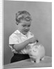 1950slittle boy putting coin into piggy bank by Anonymous