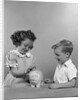 1950s little girl and boy putting coin into piggy bank by Anonymous