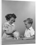 1950s little girl and boy putting coin into piggy bank by Anonymous