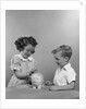 1950s little girl and boy putting coin into piggy bank by Anonymous