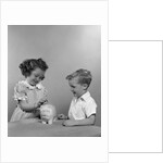 1950s little girl and boy putting coin into piggy bank by Anonymous