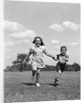 1940s two smiling children running holding hands in grassy field by Anonymous
