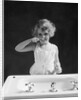 1930s child curly hair blond girl brushing teeth toothbrush looking at camera by Anonymous