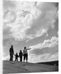 1950s 1960s family of four silhouetted on top rocky hill pointing at clouds in sky by Anonymous