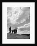 1950s 1960s family of four silhouetted on top rocky hill pointing at clouds in sky by Anonymous