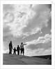 1950s 1960s family of four silhouetted on top rocky hill pointing at clouds in sky by Anonymous