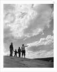 1950s 1960s family of four silhouetted on top rocky hill pointing at clouds in sky by Anonymous