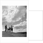 1950s 1960s family of four silhouetted on top rocky hill pointing at clouds in sky by Anonymous