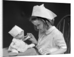 1930s little girl playing nurse with doll spoonful of medicine by Anonymous