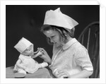 1930s little girl playing nurse with doll spoonful of medicine by Anonymous
