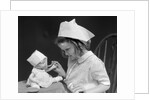 1930s little girl playing nurse with doll spoonful of medicine by Anonymous