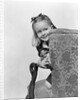 1940s little girl holding doll peeking around side of chair by Anonymous