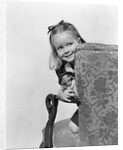1940s little girl holding doll peeking around side of chair by Anonymous
