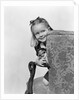 1940s little girl holding doll peeking around side of chair by Anonymous