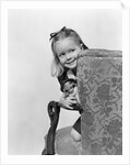 1940s little girl holding doll peeking around side of chair by Anonymous