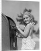 1930s 1940s child blond little girl with pigtails putting letter into mail box, looking at camera by Anonymous