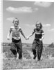 1950s boy girl running grassy farm field holding hands by Anonymous