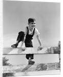 1940s brunette boy wearing overalls climbing over fence by Anonymous