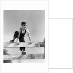 1940s brunette boy wearing overalls climbing over fence by Anonymous