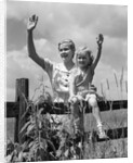 1930s girl sitting on fence with woman next to her in field waving by Anonymous