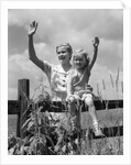 1930s girl sitting on fence with woman next to her in field waving by Anonymous