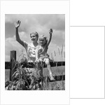 1930s girl sitting on fence with woman next to her in field waving by Anonymous