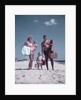 1950s family man woman mother father children boy girl son daughter standing sandy beach with toys and picnic basket by Anonymous