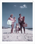 1950s family man woman mother father children boy girl son daughter standing sandy beach with toys and picnic basket by Anonymous