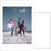 1950s family man woman mother father children boy girl son daughter standing sandy beach with toys and picnic basket by Anonymous