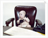 1960s chubby baby sitting in leather chair at office desk holding telephone by Anonymous