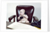 1960s chubby baby sitting in leather chair at office desk holding telephone by Anonymous