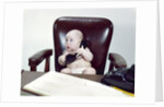 1960s chubby baby sitting in leather chair at office desk holding telephone by Anonymous