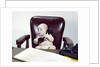 1960s chubby baby sitting in leather chair at office desk holding telephone by Anonymous