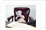 1960s chubby baby sitting in leather chair at office desk holding telephone by Anonymous