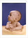 1960s portrait of baby on yellow blanket resting on folded arms head turned to right looking up by Anonymous