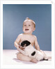 1960s smiling baby girl sitting in diapers playing with young black and white puppy dog by Anonymous