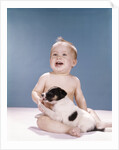 1960s smiling baby girl sitting in diapers playing with young black and white puppy dog by Anonymous
