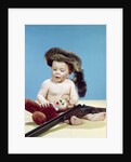 1960s baby boy wearing coonskin cap with stuffed animal and shotgun by Anonymous