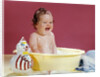 1960s crying brunette baby sitting in yellow plastic bath tub with toy clown by Anonymous