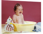 1960s crying brunette baby sitting in yellow plastic bath tub with toy clown by Anonymous