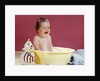 1960s crying brunette baby sitting in yellow plastic bath tub with toy clown by Anonymous