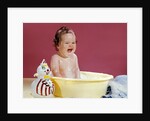 1960s crying brunette baby sitting in yellow plastic bath tub with toy clown by Anonymous