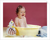 1960s crying brunette baby sitting in yellow plastic bath tub with toy clown by Anonymous