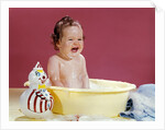 1960s crying brunette baby sitting in yellow plastic bath tub with toy clown by Anonymous