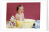 1960s crying brunette baby sitting in yellow plastic bath tub with toy clown by Anonymous